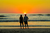 Paar hält sich am Strand von Guiones an den Händen, wo sich die Leute zum Surfen versammeln und den Sonnenuntergang beobachten, Playa Guiones, Nosara, Guanacaste, Costa Rica, Mittelamerika