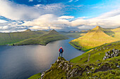 Wanderer mit Rucksack genießt die Aussicht auf den Felsen über dem Funningur Fjord, Eysturoy Island, Färöer Inseln, Dänemark, Europa