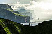 Silhouette of hikers admiring cliffs standing on top of mountain ridge above the ocean, Kalsoy island, Faroe Islands, Denmark, Europe