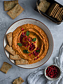 Cheese crackers with red pepper hummus and pomegranate seeds