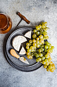 Brie and green grapes on stone plate and a glass of white wine