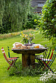 Gartentisch mit bunten Stühlen und Sommerblumen auf einer Wiese