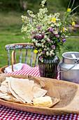 Bouquet of spring flowers in glass vase on picnic table with butter and crispbread