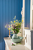 Vase with wildflower bouquet on a white chest of drawers in front of blue wood panelling