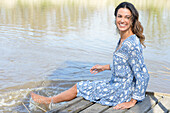 Brunette woman sitting on a wooden pier by the lake