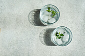 Drinking water with mint leaves and ice cubes on concrete table