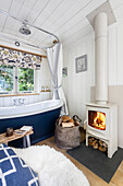 Freestanding bathtub and wood-burning stove in white bathroom with wooden ceiling