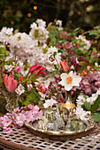 Frühlingsstrauß mit Narzisse (Narcissus), Schachbrettblume und Tulpen auf silbernem Tablett mit Mandelblüten in Parfümflacons, Zierkirschenzweig und Osterhasenfigur