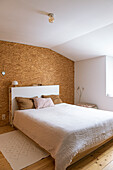 Schlafzimmer mit Wandverkleidung aus Kork und hellem Holzboden