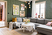 Living room with light grey corner sofa, green patterned wallpaper and gallery wall