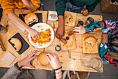 Top view of diverse crop anonymous female friends eating delicious hamburger with fries and snacks on wooden table at restaurant