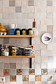 Shelves with assorted cups and tea caddies in front of tiled kitchen wall