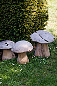 Three decorative wooden mushroom sculptures in the garden next to a hedge