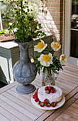 Wooden table on the terrace with strawberry cheesecake and bouquet of flowers in glass vase