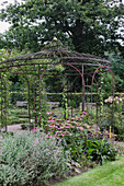 Metal pavilion with lush greenery and flowering perennials in the garden