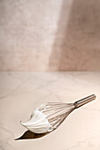 Whisk with egg foam on a marble plate