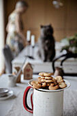 Life style scene in dining room with cookies named glagoliki on white plate which is on white table with woman s and cat s siluette and Advent calendar gift boxes as background