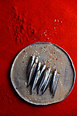 Fresh anchovies on a tray against a red background