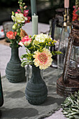 Blumenarrangement mit Zinnien (Zinnia) und Nelken (Dianthus) in grauen Vasen neben antiken Laternen