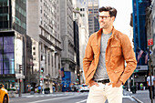 Junger Mann mit Brille in brauner Jacke auf der Straße