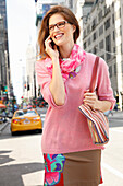 Fröhliche junge Frau mit Brille im rosa Pulli telefoniert auf der Straße