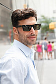 Junger Mann mit Sonnenbrille in hellem Hemd auf der Straße
