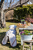 Frühlingspicknick mit Tablett auf Holztisch im Garten, Decke und Kissen
