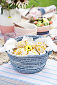 Selbstgebackene Brötchen mit Blüten in einem Korb auf einem gedeckten Tisch im Garten