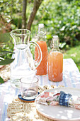 Sommerlicher Gartentisch mit Wasserkaraffe und Fruchtsaft in Bügelflaschen