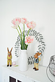 Old wooden cabinet with pastel pink tulip bouquet, wreath and Easter bunny figurines
