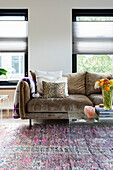 Velvet sofa with throw pillows and vase with ranunculus on glass table