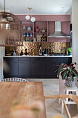 Kitchen with pink wall shelf, golden tiled backsplash and black base cabinets