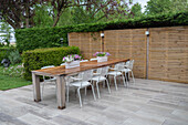 Large wooden dining table with white chairs on terrace