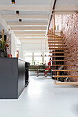 Open-plan living room with suspended staircase and brick wall