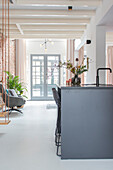 Modern open-plan kitchen with black cooking island, bar stools and view of living room with glass doors