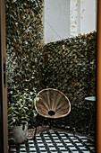 Woven chair and metal table on a small balcony with climbing plants and patterned tiles