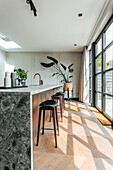 Modern kitchen with marble worktop, wooden bar stools and large window