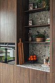 Fitted kitchen with niche shelving, marble panelling and fresh oranges on counter