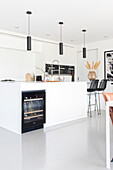 Modern white kitchen with kitchen island, integrated wine cabinet and bar stools