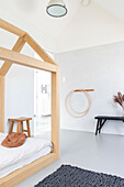 Helles Kinderzimmer mit Holzbett in Hausform, grauem Teppich und Hula-Hoop-Reifen an der Wand