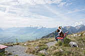 Mädchen mit Hunden auf einer Bank sitzend mit Blick auf eine majestätische, sonnige Bergkette, Schweiz