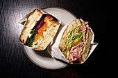 Still life gourmet sandwich halves wrapped in paper on plate\n