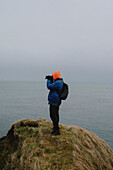 Fotograf mit Kamera auf Klippe über dem Meer, Keiss, Schottische Highlands, Schottland