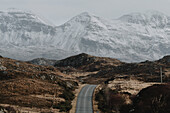 Straße unter verschneiten, majestätischen Bergen, Assynt, Sutherland, Schottland