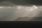 Sonnenstrahlen durch Wolken über Klippen und Meer, Sheildag, Torridon, Schottland