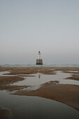 Lighthouse on sea beyond tide pools on beach, Rattray, Aberdeenshire, Scotland\n