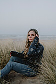 Portrait schöne junge Frau sitzt im Strandgras, Rattray, Aberdeenshire, Schottland