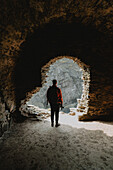 Man with backpack standing in abandoned castle archway, Findlater, Aberdeenshire, Scotland\n