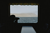 Silhouettierter Fotograf mit Kamera fotografiert Meerblick von der Fähre aus, Sandur, Färöer Inseln