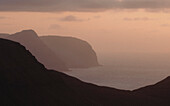 Serene pink sky over silhouetted cliffs along ocean, Klakkur, Klaksvik, Faroe Islands\n